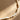 A close-up of a necklace made of irregular, organic-shaped cream-colored beads with a small gold spacer bead, laid on a textured brown surface with diagonal shadows.