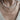 A close-up of a person's neck and chest wearing two layered necklaces. The top necklace is made of irregular white shell beads with a white shell whale tail pendant.