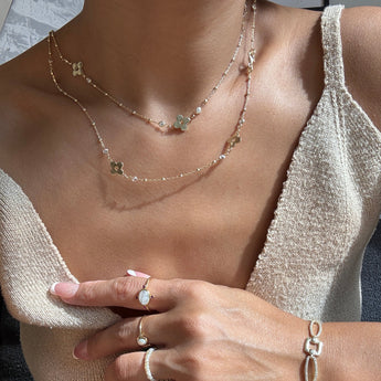 Woman wearing dainty long gold necklace with zircon flower detail.