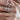 A close-up of a person's hand wearing multiple silver rings with clear stones and one ring featuring a turquoise-colored stone, along with a pearl necklace.