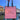 A pink paper shopping bag with black handles held by a hand, featuring the logo and name 'Amelie Jewelry Copenhagen' against a background of a canal and buildings.