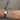 A close-up of a person's wrist wearing multiple bracelets, including two silver tennis-style bracelets, a silver watch with a metal link band, a thin gold bracelet, and a red cord bracelet, against an outdoor pavement background.