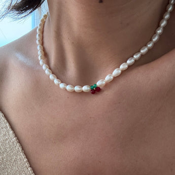 A close-up of a person wearing a white baroque pearl necklace with a small green and red decorative accent at the center.