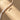 A close-up of a necklace with irregular white pearl-like beads and a gold-toned mermaid tail pendant, laid on a warm beige surface with soft diagonal shadows.