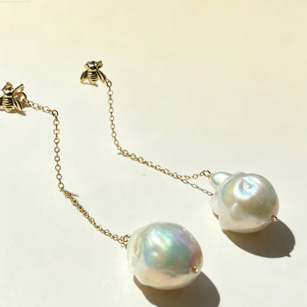Pearl earrings with gold chain on a light background