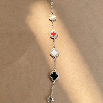 A silver chain bracelet laid flat on a warm beige background, featuring alternating oval and diamond-shaped links with red, white, and black inlays.