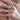 A close-up of a person's hand wearing multiple silver rings with floral and pearl-like designs, along with a delicate gold beaded necklace.