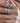 A close-up of a person's hand wearing multiple silver rings with clear stones and one ring featuring a turquoise-colored stone, along with a pearl necklace.