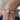 A close-up of a person's wrist wearing a beaded stretch bracelet with white baroque pearls and small red and green beads, styled with a beige knit sweater and blue jeans.