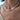 A close-up of a person wearing a white baroque pearl necklace with a small green and red decorative accent at the center.