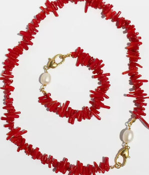 A red coral chip necklace and matching bracelet set with gold-tone clasps and white pearl accents, displayed on a light gray background.