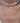 A close-up of a person's neck and chest wearing a layered necklace. The top layer features irregular white baroque pearls on a silver chain, and the bottom layer is a delicate silver chain with a small white textured pendant.