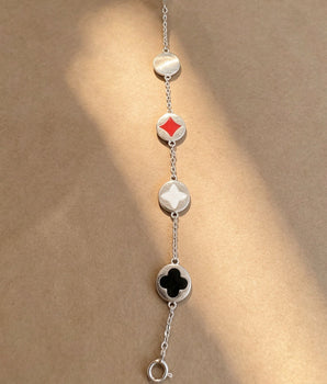 A silver chain bracelet laid flat on a warm beige background, featuring alternating oval and diamond-shaped links with red, white, and black inlays.