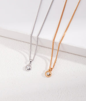 Delicate minimalist zircon pendant necklace on a gold chain, styled in a flat lay for everyday elegance. Features a sparkling round-cut stone with adjustable 40cm+6cm length.