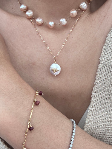 Pearl necklace and bracelet on a person wearing a light-colored top.